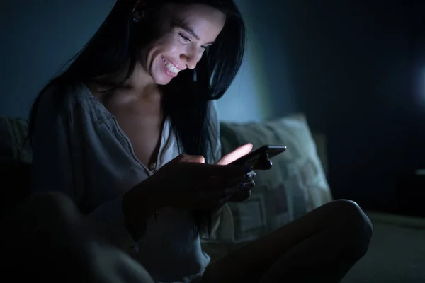 Mosolygó nő használ smartphone, este sötét szobában, online társkereső szolgáltatás — Stock Fotó