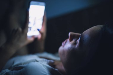 Gece uyku önce mavi perde-in akıllı telefon kullanan kadın