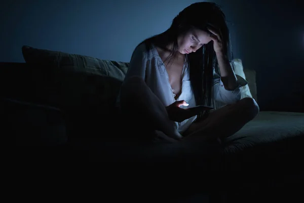 Уставшая женщина с синим экраном смартфона ночью в темной комнате — стоковое фото