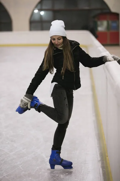 Νεαρή γυναίκα να στέκεται στον πάγο από ένα παγοδρόμιο στερεώνει τα πατίνια — Φωτογραφία Αρχείου