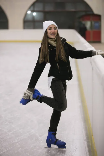 Junge Frau steht auf dem Eis einer Eisbahn und schnallt ihre Schlittschuhe an — Stockfoto