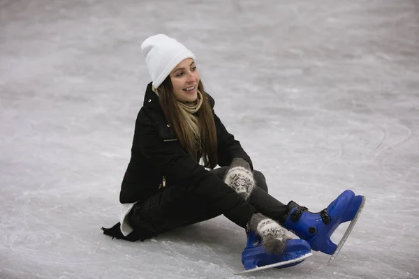 Jovem mulher feliz sentada no gelo de uma pista de patinação — Fotografia de Stock