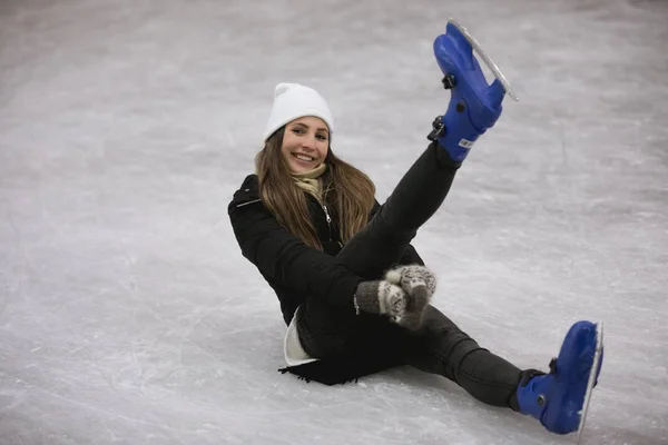 Jeune femme heureuse assise sur la glace d'une patinoire — Photo