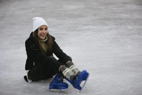 Young woman sitting on ice of a skating rink fastens her skates