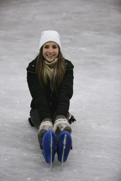 Jeune femme heureuse assise sur la glace d'une patinoire — Photo