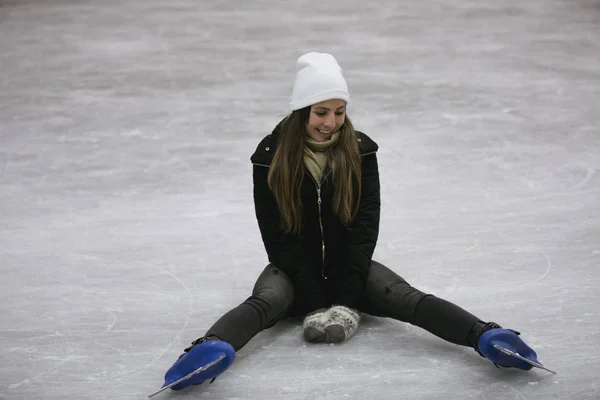 Joven mujer feliz sentada en el hielo de una pista de patinaje —  Fotos de Stock
