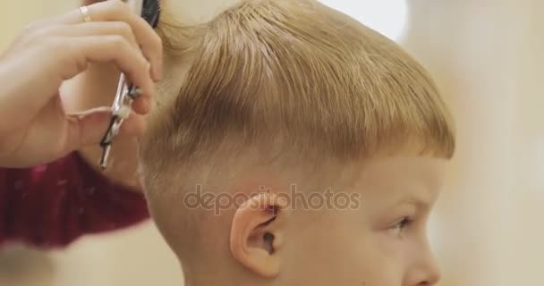 Peinado infantil. Primer plano del corte de pelo de niño en el salón usando tijeras y peine . — Vídeos de Stock