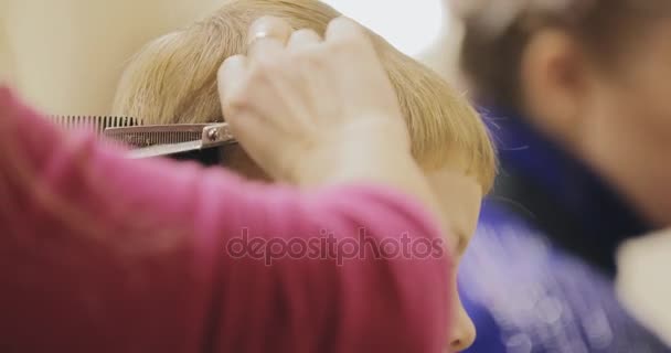 Coiffure d'enfant. Gros plan de la coupe de petit garçon dans le salon à l'aide de ciseaux et peigne . — Video