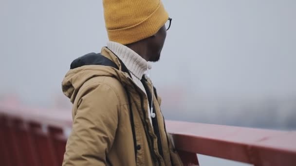 Fiatal fekete férfi sapka, nemhogy arra gondolt egy hídon — Stock videók