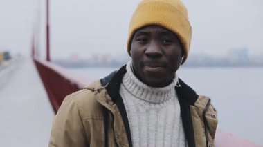 Genç gülümseyen adam resme bir köprü üzerinde soğuk kış duran siyah kulaklık dinle