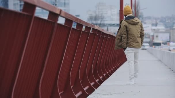 Νέοι μαύρο άνδρα στο κρύο χειμώνα ακούγοντας μουσική περπάτημα σε μια γέφυρα — Αρχείο Βίντεο