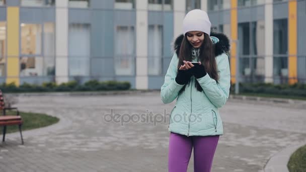 Chica de pie y hablando por teléfono inteligente en el patio del edificio en invierno — Vídeos de Stock