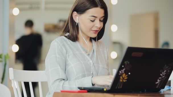 Mujer blogger trabajando en cafetería usando laptop y escuchando música — Vídeo de stock