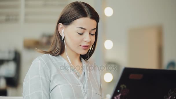 Mujer blogger trabajando en cafetería usando laptop y escuchando música — Vídeo de stock