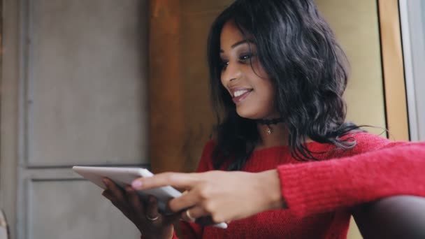 Улыбающаяся чернокожая женщина с сенсорным экраном планшетного компьютера сидит в кафе — стоковое видео