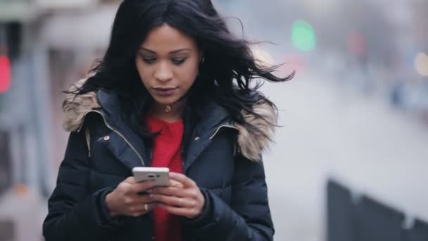 Mujer joven caminando en la calle en invierno utilizando la pantalla táctil del teléfono inteligente — Vídeos de Stock