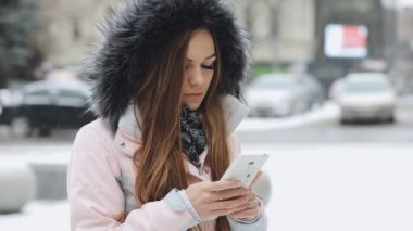 Karlı kış gününde akıllı telefon mobil cihaz kullanan genç kadın