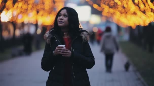 Hermosa mujer caminando bebiendo té en el callejón decorado con luces de la ciudad — Vídeo de stock