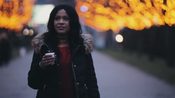 Hermosa mujer caminando bebiendo té en el callejón decorado con luces de la ciudad — Vídeos de Stock