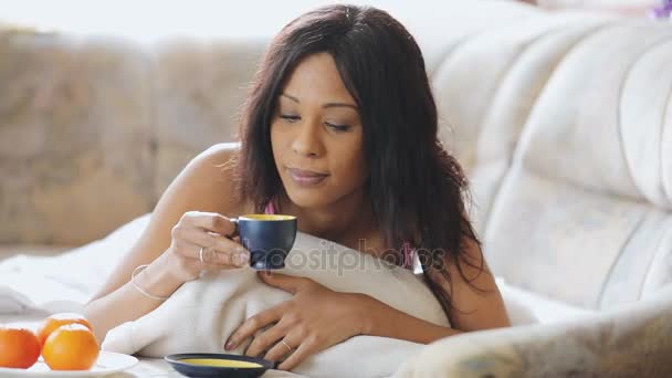 Mujer morena en la cama cómoda bebiendo taza de té en casa — Vídeos de Stock