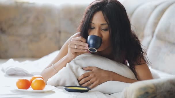 Mujer morena en la cama cómoda bebiendo taza de té en casa — Vídeos de Stock