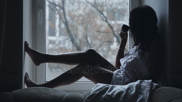 Mujer sentada en un alféizar de la ventana beber té, ella soñando — Vídeos de Stock