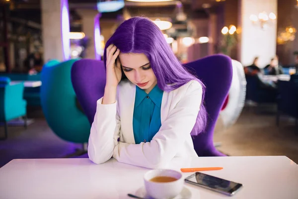 Tired extraordinary business woman with purple hair sitting in a futuristic cafe