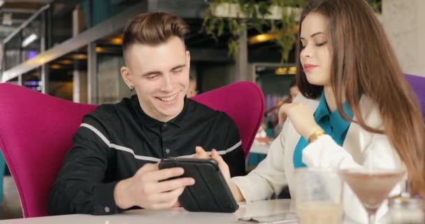 时尚的年轻情侣在咖啡馆里聊天, 一起看平板电脑 — 图库视频影像
