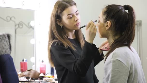 Visagista haciendo maquillaje para chica modelo en el salón — Vídeo de stock