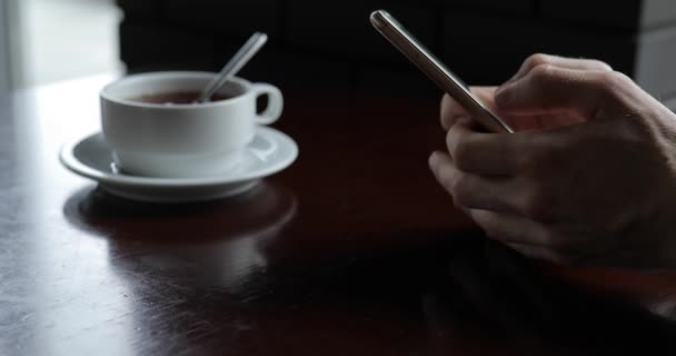 Мужская рука с помощью смартфона, пока чай охлаждается — стоковое видео