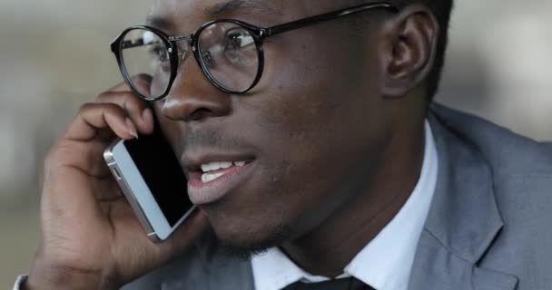 Африканский бизнесмен разговаривает по смартфону в кафе крупным планом — стоковое видео