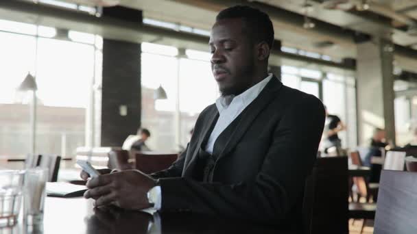 Африканский бизнесмен пользуется сенсорным экраном смартфона в кафе — стоковое видео