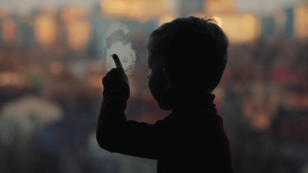 Silhouette of little boy drawing human face on a window — Stock Video