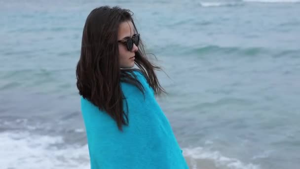 Femme en serviette bleue debout sur fond de vagues de mer, vent soufflant les cheveux — Video