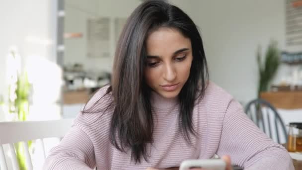 Красива жінка, використовуючи додаток для смартфона, сидить у кафе — стокове відео