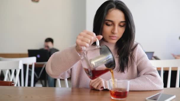 Mulher bonita derramando chá de chaleira em vidro em um café — Vídeo de Stock