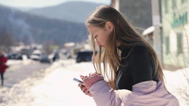 Женщина использует смартфон на зимней улице города в замедленной съемке — стоковое видео
