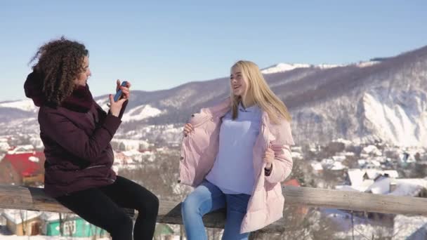 Two girls friends photographing each other on snowy mountains background — Stock Video