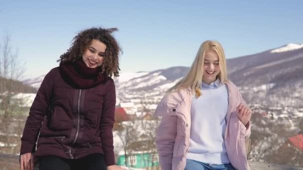 Dos chicas amigas divirtiéndose, tirar nieve a la cámara con las piernas — Vídeos de Stock