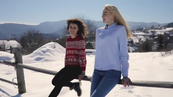 Happy young women friends sitting on fence, snowy mountain landscape around — Stock Video