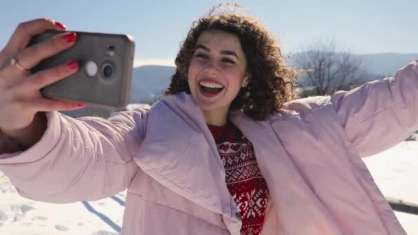 幸せな巻き毛の女は雪に覆われた山の風景をビデオ モバイルの selfie を作る — ストック動画