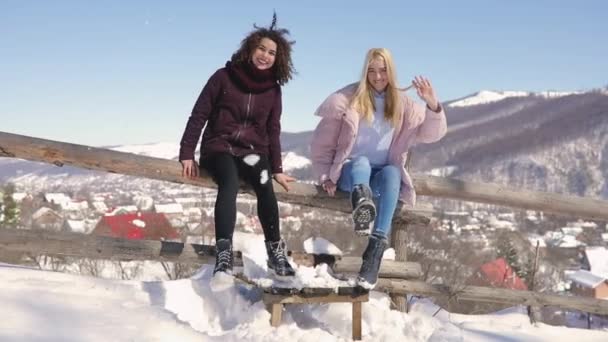Κορίτσι φίλοι διασκεδάζουν, ρίχνουν χιόνι στη φωτογραφική μηχανή κάθεται στο φράχτη — Αρχείο Βίντεο