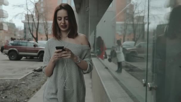 Woman listening to music in city looking down to smartphone — Stock Video