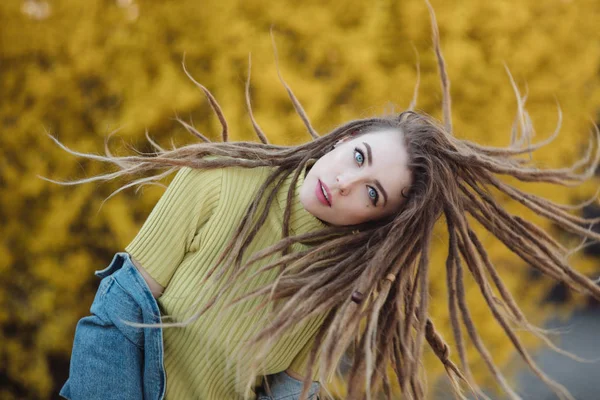 Hair toss, woman with dreadlocks against yellow shrub background