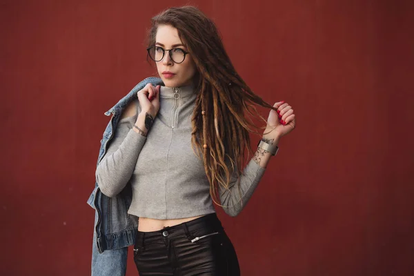 Mulher elegante com dreadlocks posando contra fundo da parede vermelha — Fotografia de Stock