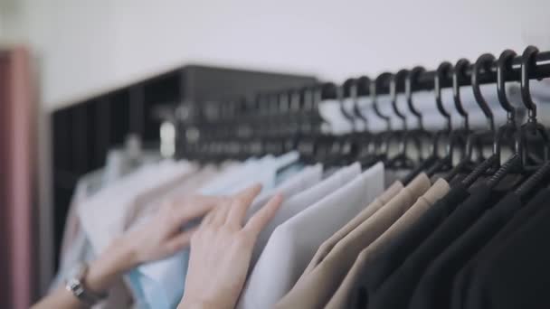 Fila de roupas em cabides na loja, as mãos femininas escolhem o desgaste — Vídeo de Stock