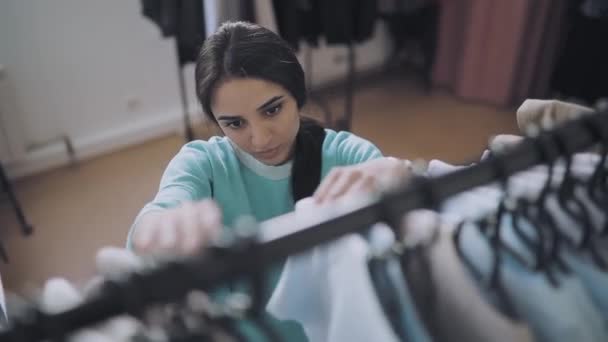 Молода жінка вибирає одяг у шоу-румі — стокове відео