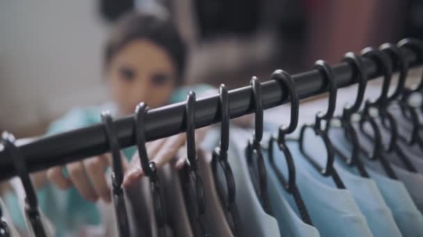 Frau wählt Kleidung im Geschäft, Fokus auf Kleiderbügel — Stockvideo