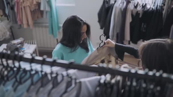 Женщина выбирает одежду в магазине, продавец помочь ей — стоковое видео