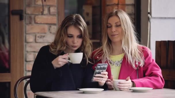 Женщины-друзья сидят в кафе и смотрят фотографии в смартфоне — стоковое видео